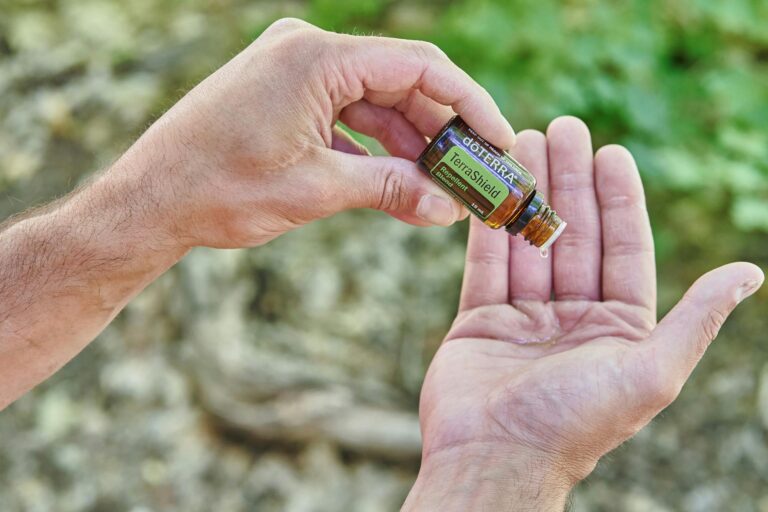 Hands pouring doterra TerraShield essential oil in a natural outdoor setting.